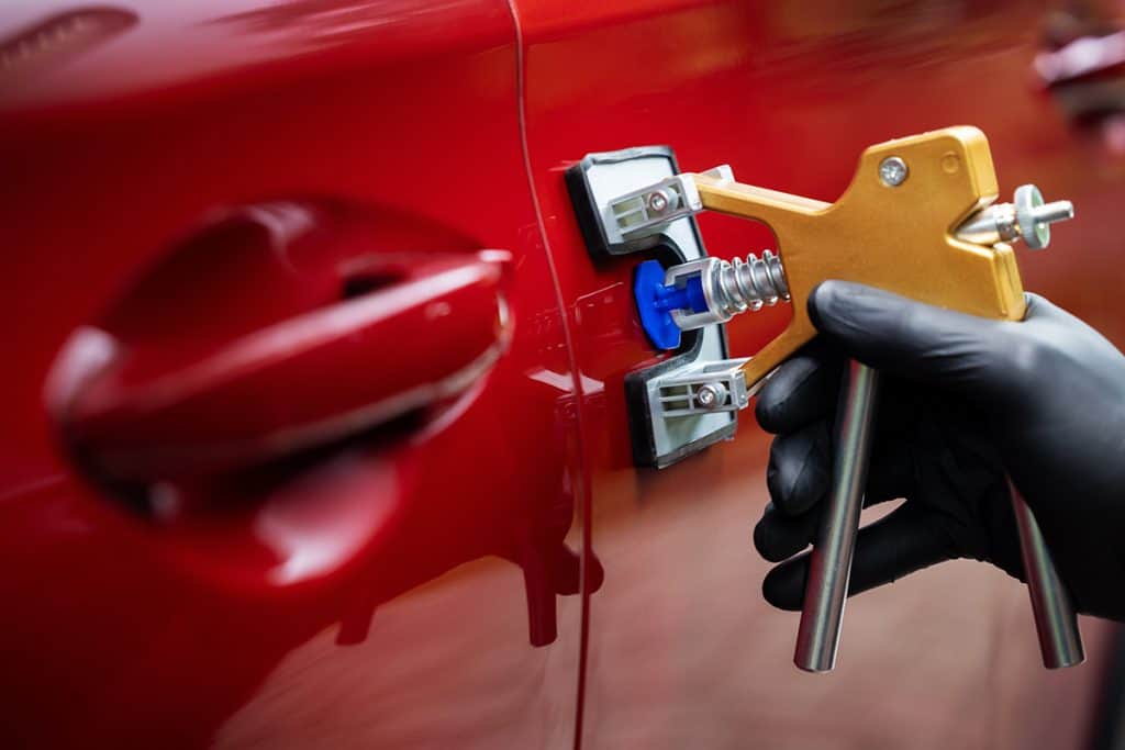 Paintless dent repair glue puller removing a dent from a red car door